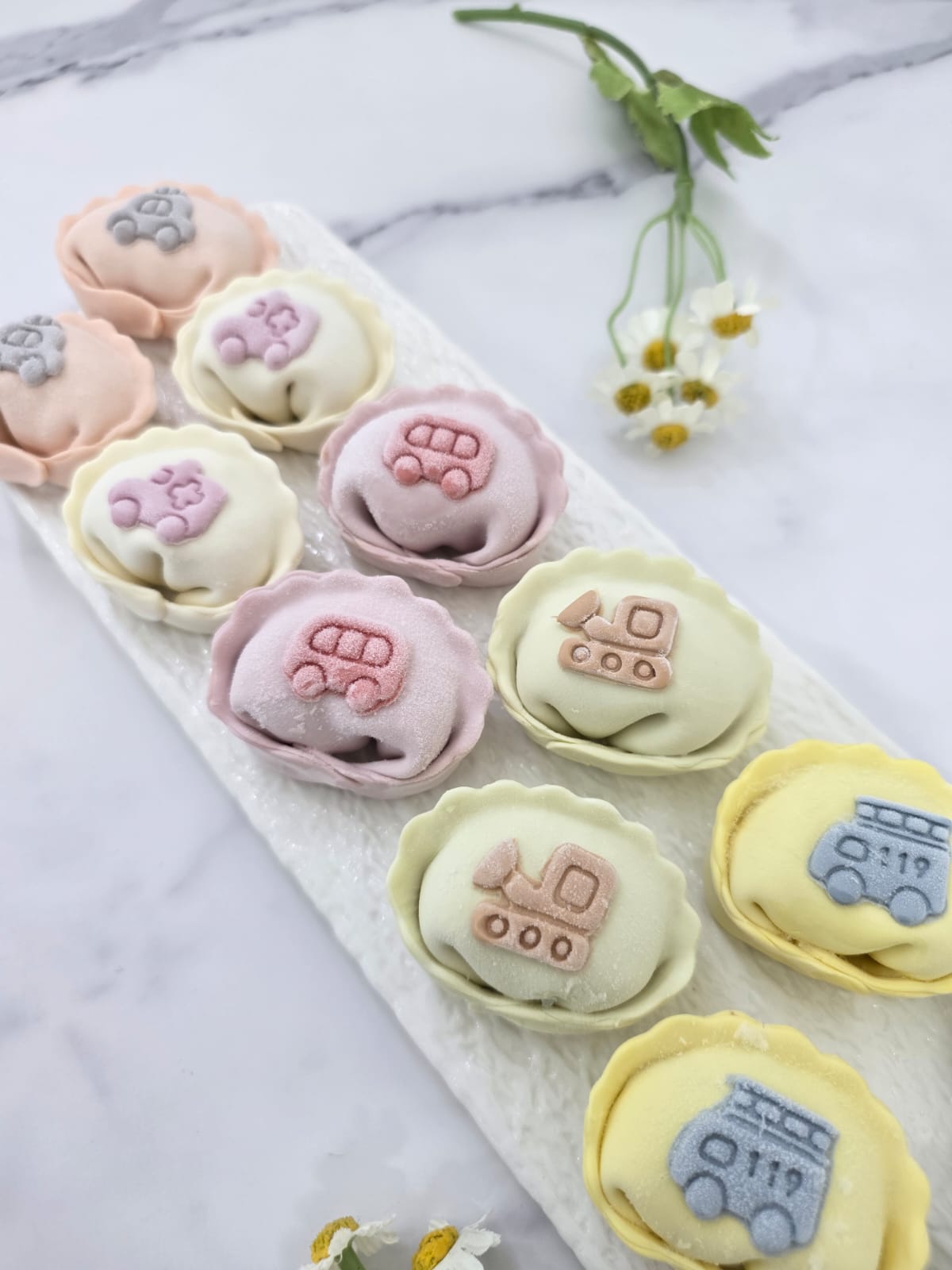 Pastel-colored Chinese dumplings with varies vehicle designs on a marble surface.