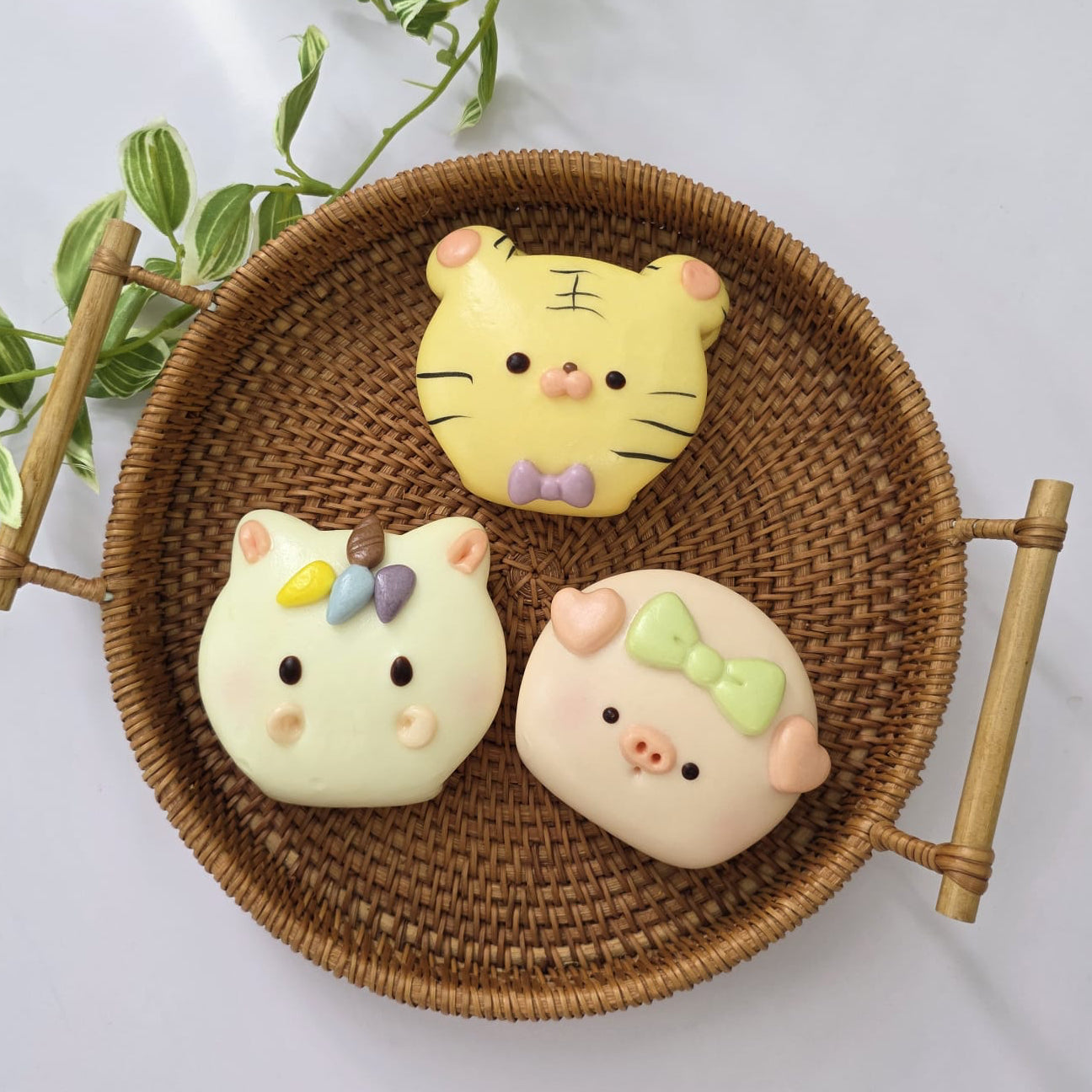 Three cartoon-style buns in a woven basket with a light gray background and green leaves.