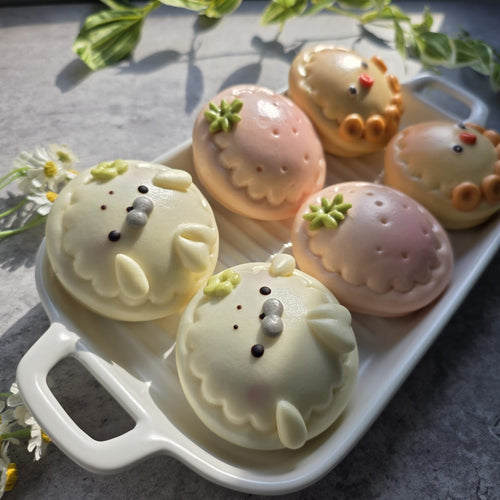 Decorative animal-shaped chocolate buns on a white tray with greenery in the background.