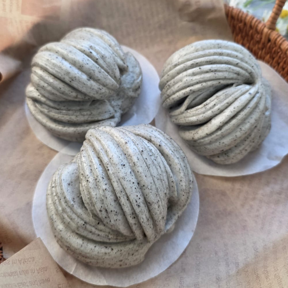 Three braided bread rolls on white paper with a woven basket in the background.